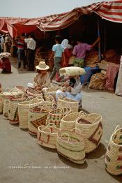 Image du Maroc Professionnelle de  Une femme étale ses paniers en osier à même le sol sur la fameuse place Jemaa El Fana de Marrakech, en espérant le passage de touristes, mais à cette heure où le soleil est au zénith le lieu est presque vide, s'abriter du soleil est une nécessité pour un bon nombre de résidents de la ville touristique du Maroc, Jeudi 19 Mai 1988. (Photo / Abdeljalil Bounhar)